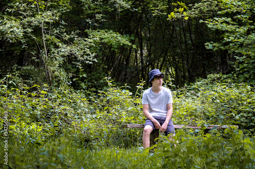 A teenage boy sits in the woods wearing a Barbour hat in Suffolk England.