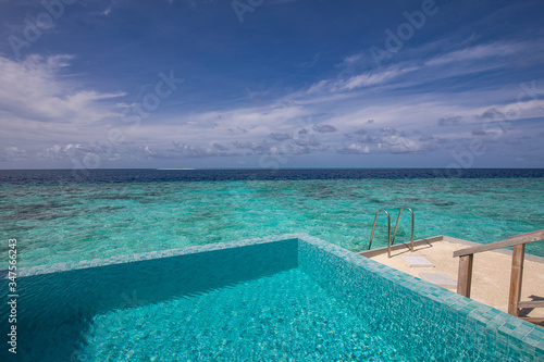 Infinity pool with sea view on the bright summer day. Luxury resort view from over water villa  endless swimming pool with stirs and ladder into ocean lagoon. Exotic summer background  hotel view