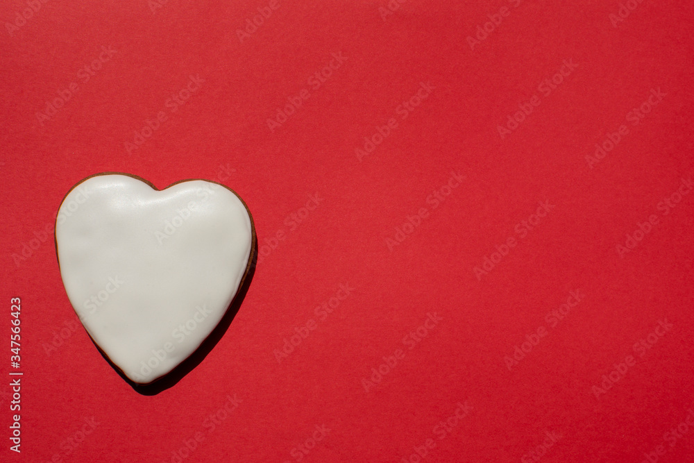 Fototapeta premium Pretty handmade gingerbread cookie covered with icing on the bright red background. Romantic banner. Copy space. Top view.