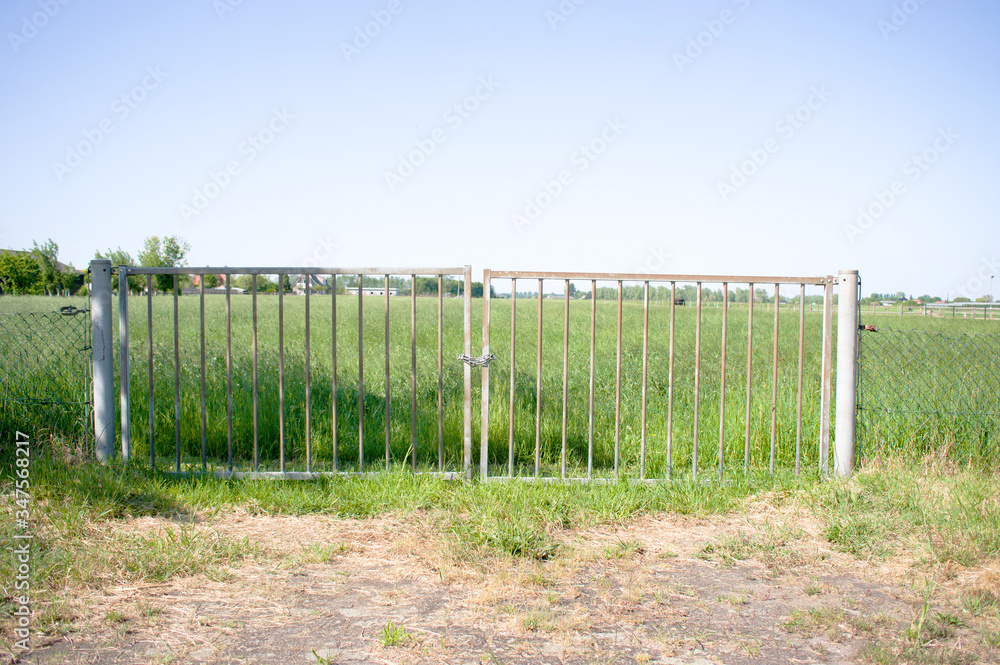 Closed gate that gives access to a path to a green meadow