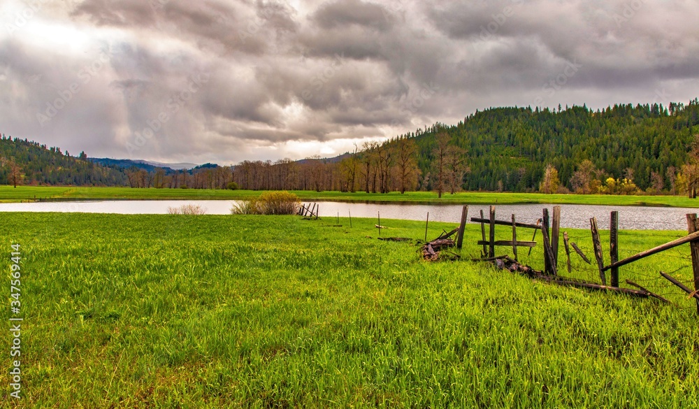Pond and fence in green field with mountain and clouds background