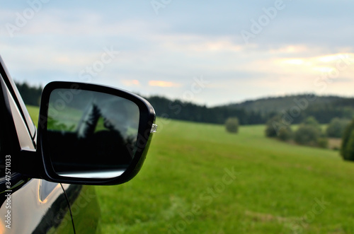 Front rear view mirror of modern black SUV crossover car vehicle in nature.