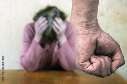 A man's clenched fist threatening with blurred view of unhappy crying woman covering her face on the background