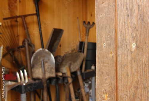 Shed with old gardening tools. Shovels, rakes, and trowels in the background. 