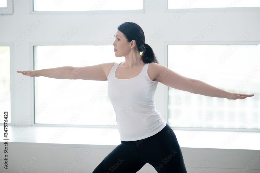 Brunette female standing in warrior pose with arms parallel to the floor Brunette female standing in warrior pose with arms parallel to the floor