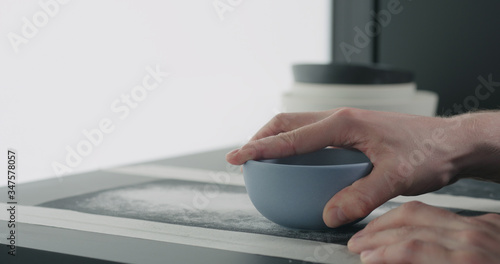 man hands sand bottom of blue ceramic bowl