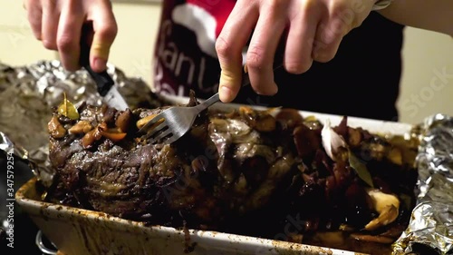 female hands cut beef roast meat on kitchen worktop at home