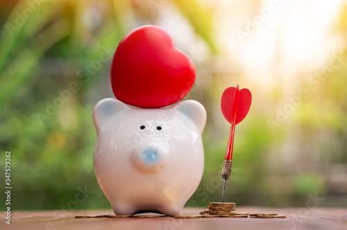 Piggy bank with red heart on the top and an arrow embroidered on a pile of coins for Investment goals in the backyard, Saving money for business plan and spending concept. photo