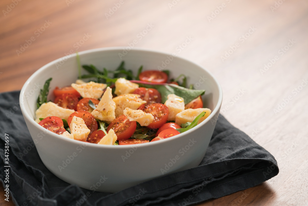 salad with cherry tomatoes, mixed grens and cheese in white bowl on wood table salad with cherry tomatoes, mixed grens and cheese in white bowl on wood table