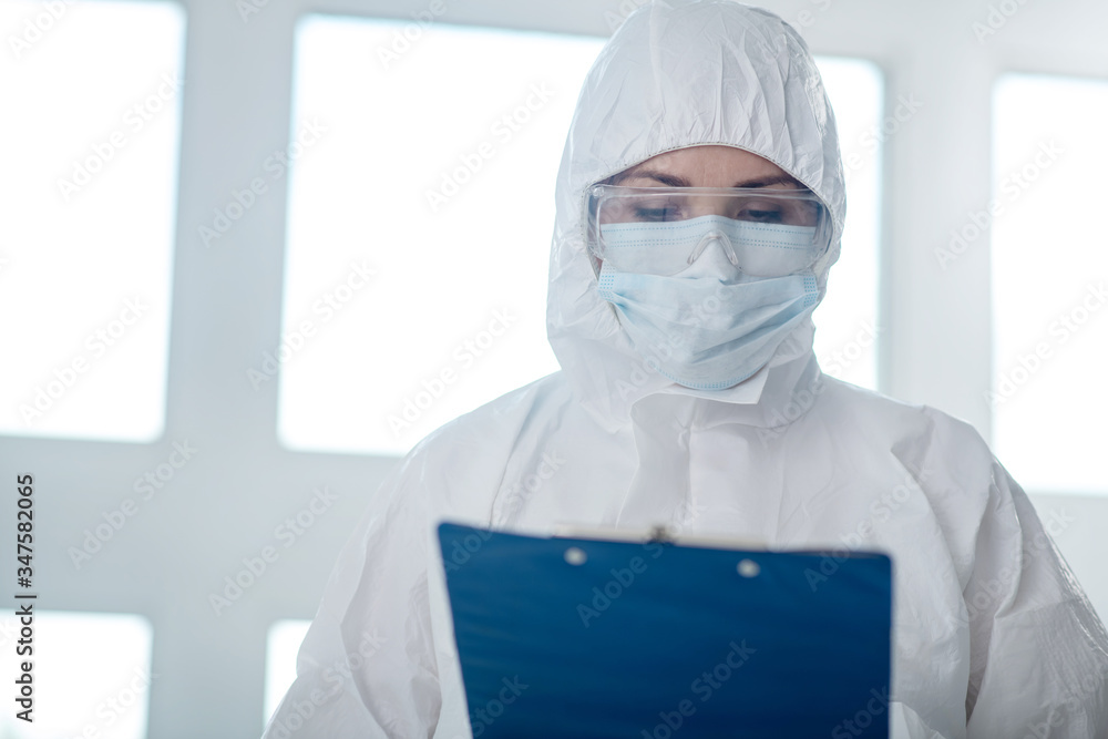 Medical worker in protective clothing, medical mask and goggles looking at clip folder Medical worker in protective clothing, medical mask and goggles looking at clip folder