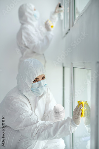 Medical workers in protective clothing and medical masks disinfecting window