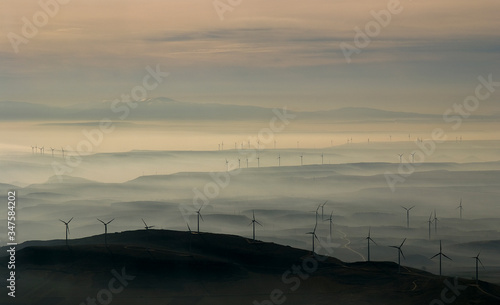 Panorámica aérea  al amanecer  de una mañana de invierno con los molinos de viento surgiendo entre la niebla  