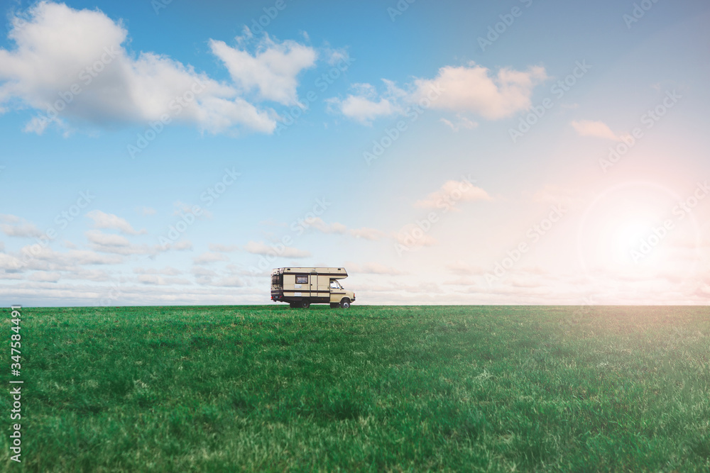 Camper van in the green field on background of blue sky with clouds. Motorhome on nature. Travelling