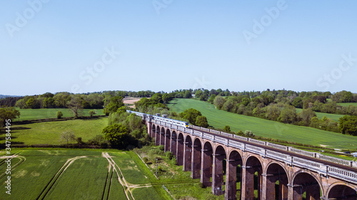 Aerial photo of a viaduct bridge with train passing through in the British countryside