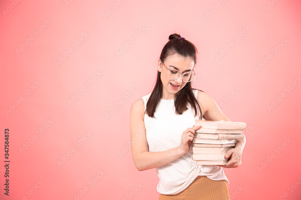 Portrait of a young woman with glasses on a pink background with books in her hands . Portrait of a young woman with glasses on a pink background with books in her hands .