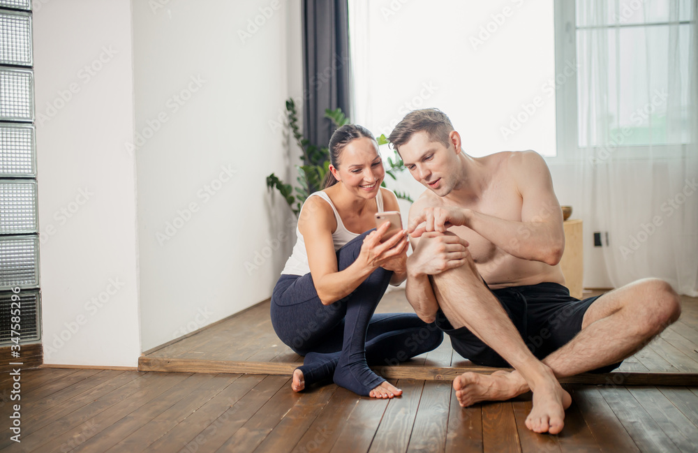 fitness woman show videos on smartphone to man, sporty couple at home, have rest after yoga workout exercises, isolated in light room fitness woman show videos on smartphone to man, sporty couple at home, have rest after yoga workout exercises, isolated in light room