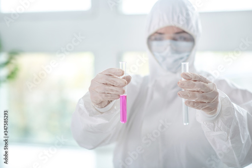 Disinfecting worker in protective workwear holding test tubes