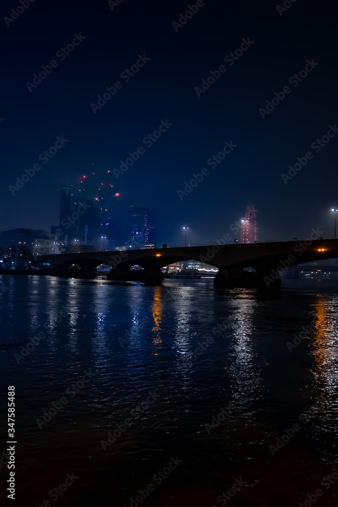 Moody foggy London night scene of bridge and lights reflected at night