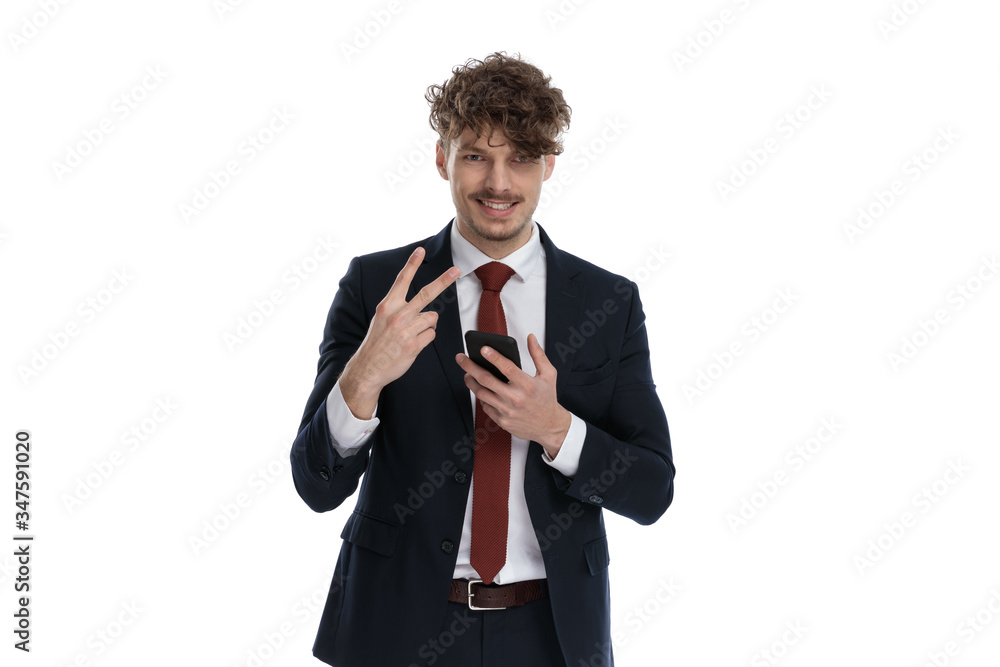 Positive businessman holding phone, smiling and gesturing peace Positive businessman holding phone, smiling and gesturing peace