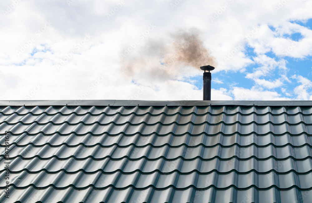 Smoke from a chimney against a blue sky. Pipe with smoke on the metal roof