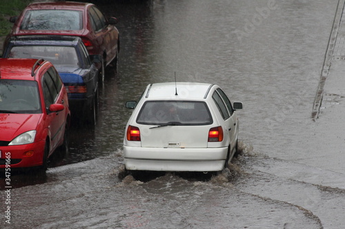 The car is driving through a large puddle in the yard during heavy rain in the city on parked vehicles background, rear top view