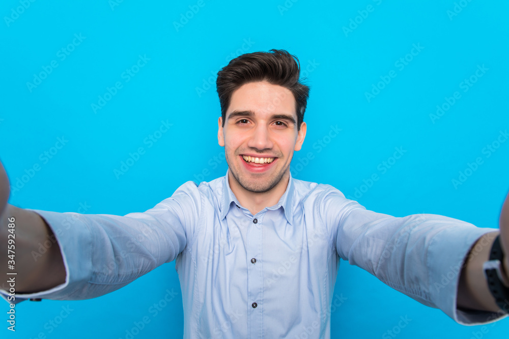 Handsome young man is making selfie and smiling on blue background Handsome young man is making selfie and smiling on blue background