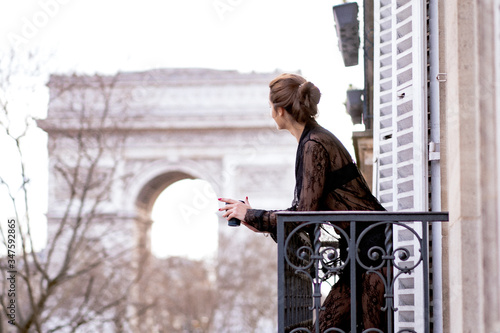 Foto Attractive  yang woman in pajama is drinking coffee on balcony in the morning in city Paris