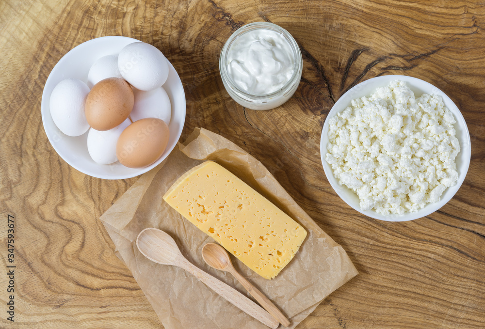 Rustic products on a textured wooden table: cottage cheese, eggs, sour cream and cheese. Healthy food, a source of useful natural calcium and vitamin D