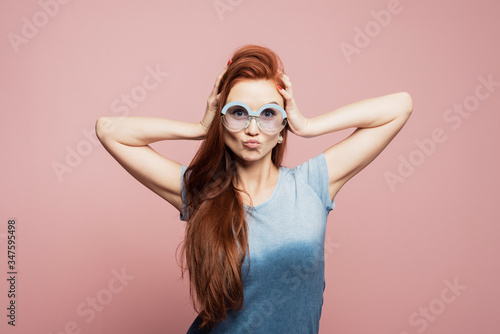 Stunning female model posing with joy face expression on pink background. Portrait of surprised young woman in sunglasses jumping in front of pink wall