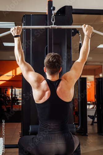 Shoulder pull down machine. Fitness man working out lat pulldown training at gym. Upper body strength exercise for the upper back. Muscular build athlete exercising on pull down weight machine