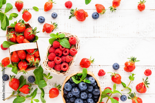 Various fresh berries in basket on white wooden background  top view. Concept of summer food. Flat lay  copy space.