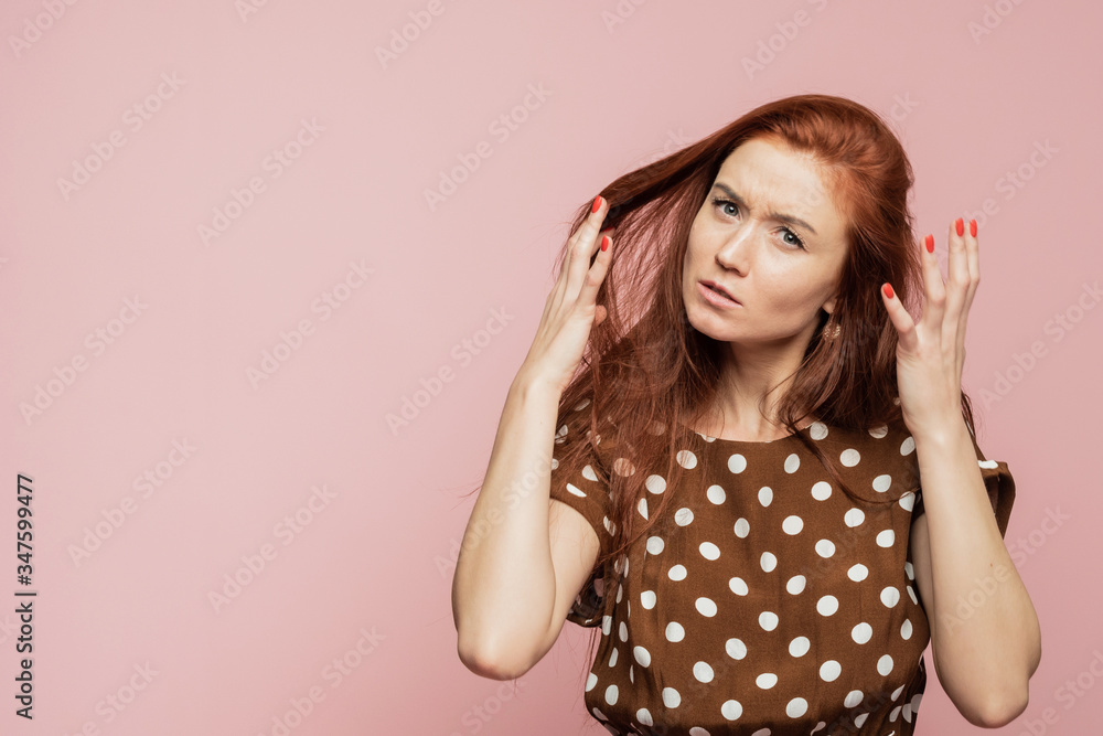 The red-haired girl is surprised and shocked. Woman experiences an emotion of rage on a pink background in the studio The red-haired girl is surprised and shocked. Woman experiences an emotion of rage on a pink background in the studio