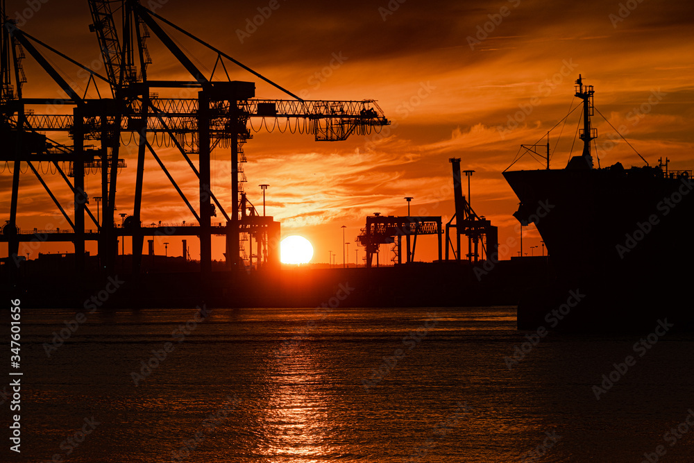 Profile of a large ship and container cranes at sunset.