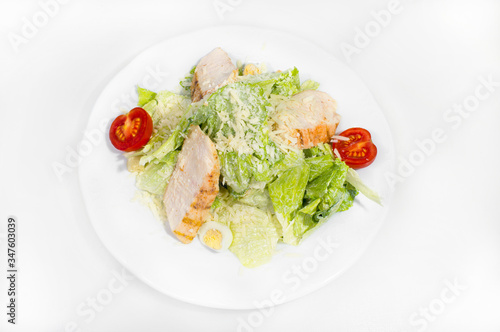 Lettuce and young cabbage salad with slices of grilled pork garnished with grated cheese, quail eggs and tomatoes on a white plate not white background