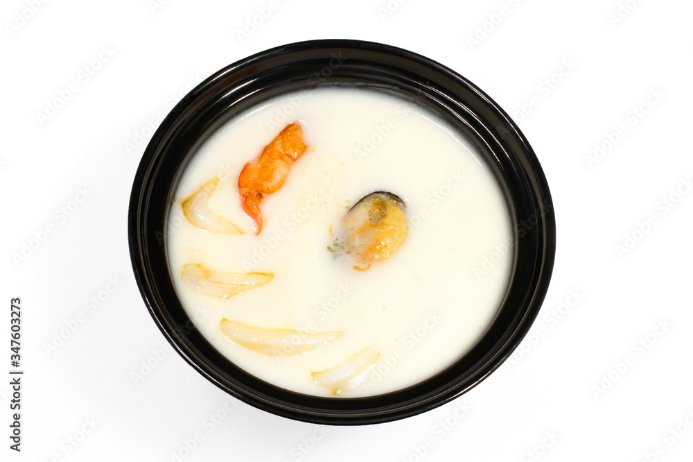 Puree milk soup with shrimps and mussels in a black deep plate on a white background Puree milk soup with shrimps and mussels in a black deep plate on a white background