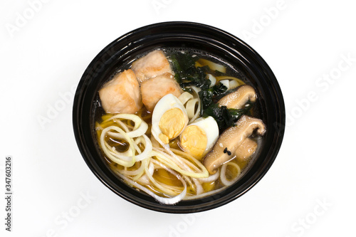 Pork noodles soup with mushrooms and seaweed with eggs and fresh onion rings in a black deep plate on a white plate