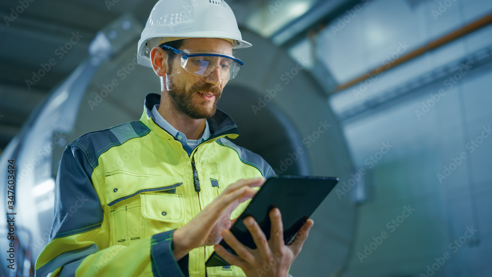 Portrait of Professional Heavy Industry Engineer / Worker Wearing Safety Uniform and Hard Hat Uses Tablet Computer. In the Background Construction Factory for Oil, Gas and Fuels Transport Pipeline Portrait of Professional Heavy Industry Engineer / Worker Wearing Safety Uniform and Hard Hat Uses Tablet Computer. In the Background Construction Factory for Oil, Gas and Fuels Transport Pipeline