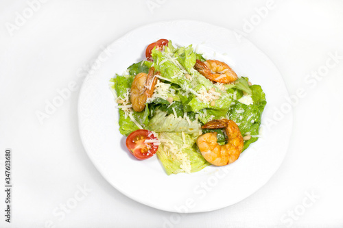 Salad of lettuce, young cabbage, shrimp and grated cheese, as well as a tomato on a white round plate on a white background