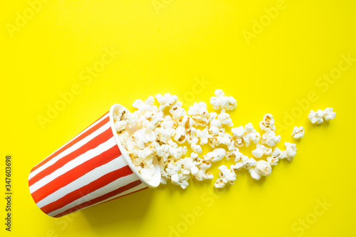 Paper Cup with drawn red stripes and scattered popcorn on a bright yellow background top view and copy space