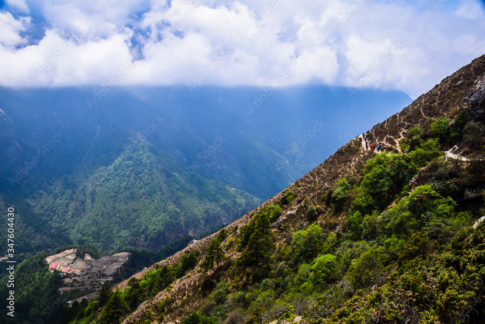 mountain landscape with clouds group of people trekking on road right side and town on left side mountain landscape with clouds group of people trekking on road right side and town on left side