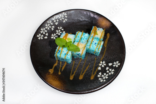 Sweet rolls of rice, baban and kiwi are sprinkled with syrup and sprinkled with blue coconut flakes on a black round plate on a white background photo