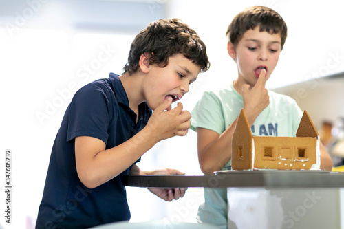 Two boys tasting and making a gingerbread house in the kitchen