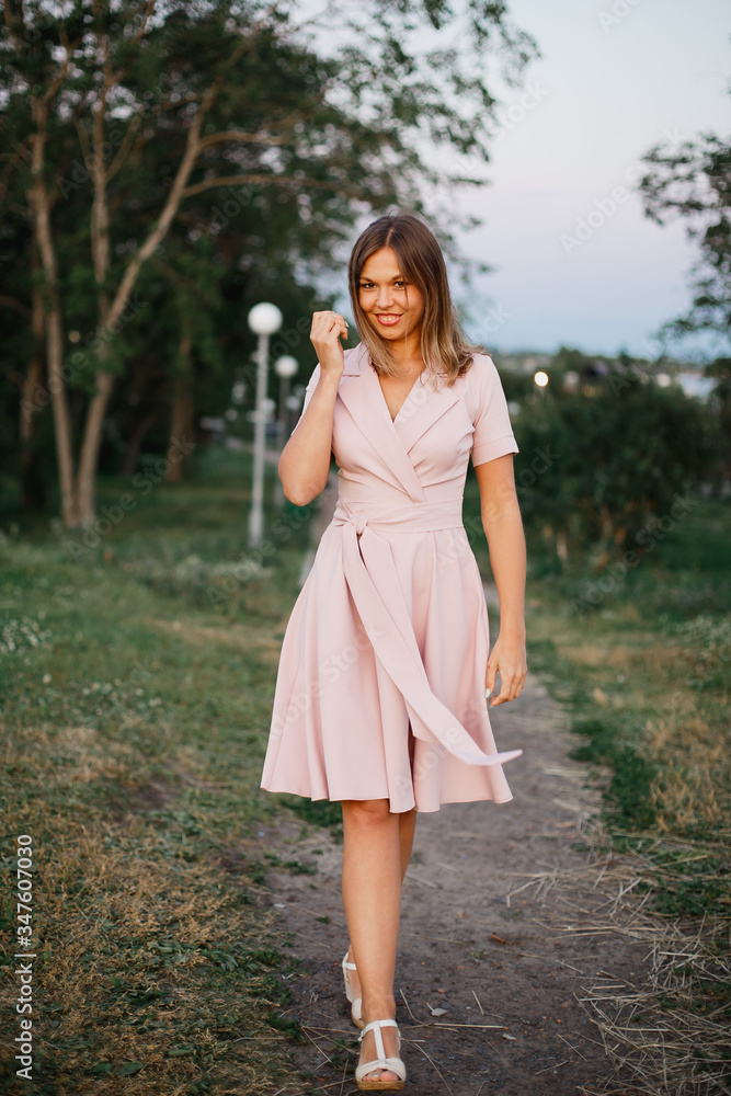 Playful young woman in pink summer dress enjoys a walk in spring park in the evening. Playful young woman in pink summer dress enjoys a walk in spring park in the evening.