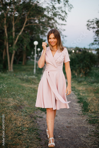 Playful young woman in pink summer dress enjoys a walk in spring park in the evening.