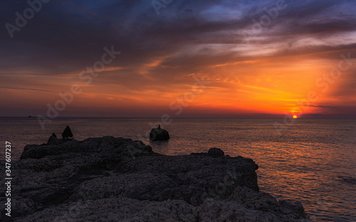 Sunset on the sea with fishermen on the shore. Seascape at sunset with beautiful clouds. Silhouettes of clouds. Panorama of a beautiful cloudy sunset over the sea.