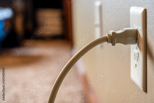 Side view of white power cord plugged into a white wall outlet photo