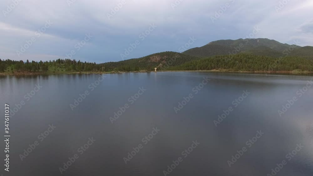 Aerial view of beautiful calm lake against cloudy sky, drone approaching structure on lakeshore against mountains - Lake Wellington, Colorado Aerial view of beautiful calm lake against cloudy sky, drone approaching structure on lakeshore against mountains - Lake Wellington, Colorado