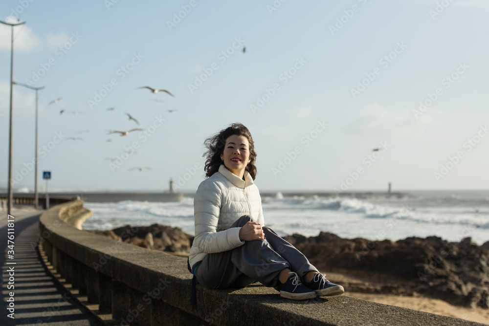 Asian woman sits on the waterfront during the surf. Porto, Portugal.