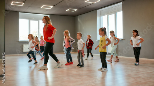 Fototapeta Naklejka Na Ścianę i Meble -  Learning how to move. Group of little boys and girls dancing while having choreography class in the dance studio. Female dance teacher and children