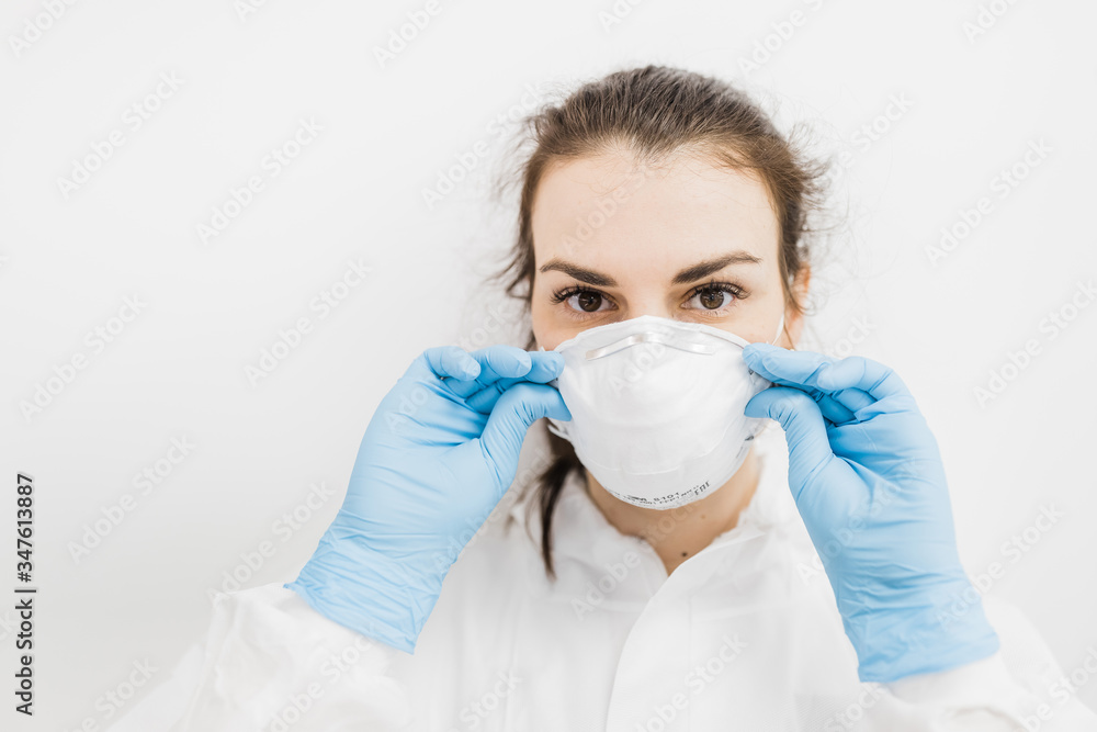 The girl doctor puts on a white protective medical mask in blue gloves on a white background.